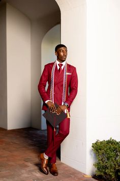 a man in a red suit and white shirt is leaning against a wall with his hands on his hips