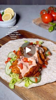 a tortilla topped with chicken, lettuce and tomatoes on a cutting board