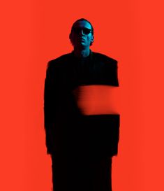 a man in a black suit and sunglasses standing against a red background with his hands on his hips