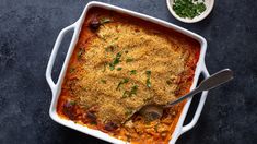 a casserole dish with meat and cheese on the side next to a spoon