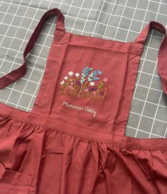 a red apron with flowers on it sitting on top of a piece of cloth next to a cutting board