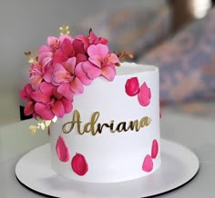 there is a white cake with pink flowers on the top and gold lettering above it