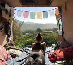 a woman sitting on top of a bed in a camper next to a forest