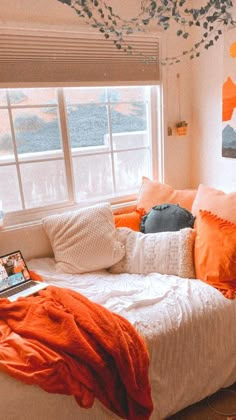 an orange and white bedroom with a laptop on the bed in front of a window