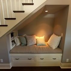 a room that has some drawers under the stairs and a bench with pillows on it