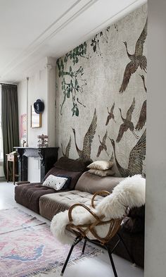 a living room filled with furniture next to a wall covered in bird paintings and rugs