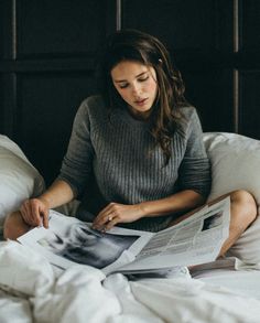 black and white photograph of a woman sitting on her bed reading a magazine while looking at the pages