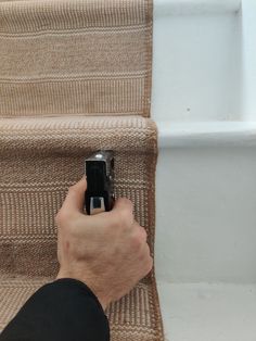 a person holding a cell phone up against the side of a stair case on top of a carpeted staircase