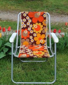 an orange and brown lawn chair sitting in the grass next to some tulips