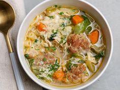 a bowl of soup with meatballs, carrots, and noodles on a table