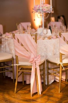 two chairs with pink sashes and bows on them are set up for a wedding reception