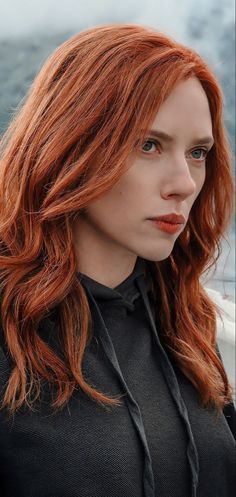 a woman with red hair and blue eyes looks off into the distance while standing on a boat