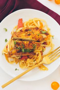 a white plate topped with pasta and meat next to a fork on top of a table