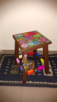 a child's wooden stool with brightly colored flowers on the top and colorful pegs underneath it