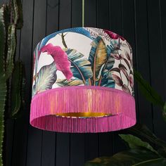 a pink lamp shade hanging from a ceiling next to a green plant and wooden wall