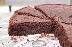 a chocolate cake is cut into pieces on a glass platter with a serving spoon