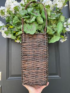 a hand holding a wicker basket with white flowers in front of a black door