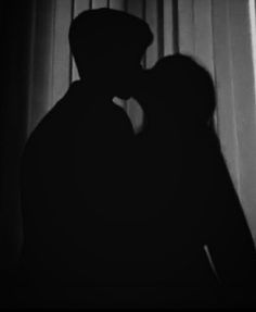 the silhouette of a man and woman kissing in front of a window with white curtains