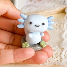 a hand holding a tiny white toy with blue wings on it's head and eyes