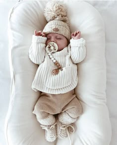 a baby sleeping in a beanie and sweater on top of a white pillow with a button