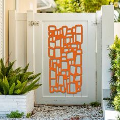 an orange piece of art sitting in front of a white fence and potted plants