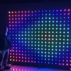 a man standing in front of a large display of colorful lights on a black wall