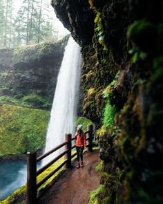 a woman is standing in front of a waterfall and looking at the water coming from it