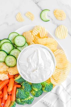 a plate with chips, broccoli, carrots and cucumbers on it