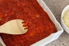 a wooden spoon in a white container filled with sauce and rice next to a bowl of pasta