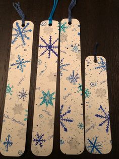 three snowflakes are hanging from the top of wooden tags on a table