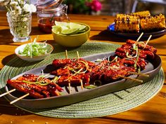 several skewered meats are on a platter with other foods in bowls