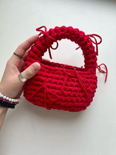 a hand holding a red crocheted purse on top of a white table next to a wall