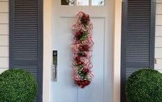 a wreath is hanging on the front door of a house with blue shutters and green topiary