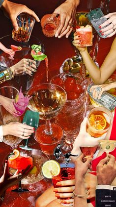 a group of people sitting around a table filled with drinks and cocktails, all holding their hands in the air