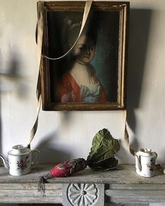 a painting hanging on the wall above a mantle with cups and saucers next to it