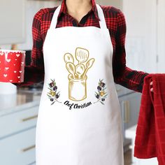 a woman wearing an apron holding a red mug and cooking utensils in her hand