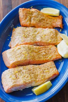 three salmon fillets on a blue plate with lemon wedges