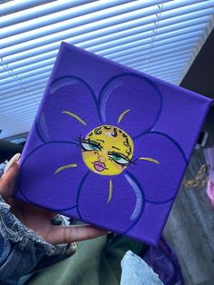 a person holding up a purple square with a yellow flower painted on it