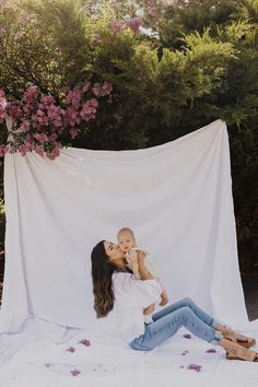 a woman holding a baby in her arms while sitting on the ground next to a blanket