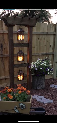 an outdoor garden with flowers and lights in the back yard, next to a wooden trellis