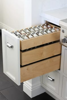 an open drawer in a kitchen with white cabinets and drawers on the bottom, filled with cans