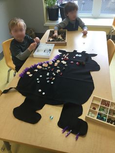 two children sitting at a table with an animal made out of t - shirts and beads