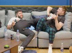 two men sitting on a couch playing video games with remote controllers and water bottles in front of them