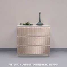 a white and beige striped dresser with a vase on top, next to the wall