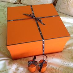 an orange gift box sitting on top of a bed with baby shoes next to it