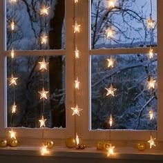 an open window with christmas lights hanging from the windowsill and snow covered trees in the background