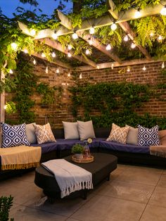 an outdoor seating area is lit up with string lights and greenery on the roof