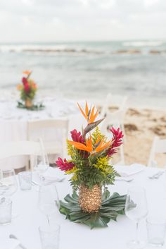 an arrangement of tropical flowers in a pineapple vase on a table at the beach