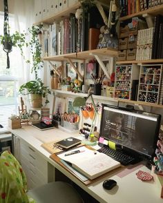 a desk with a computer, books and plants on it in front of a window