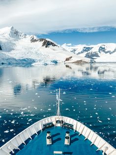 the bow end of a boat traveling past icebergs and snow covered mountains in the distance